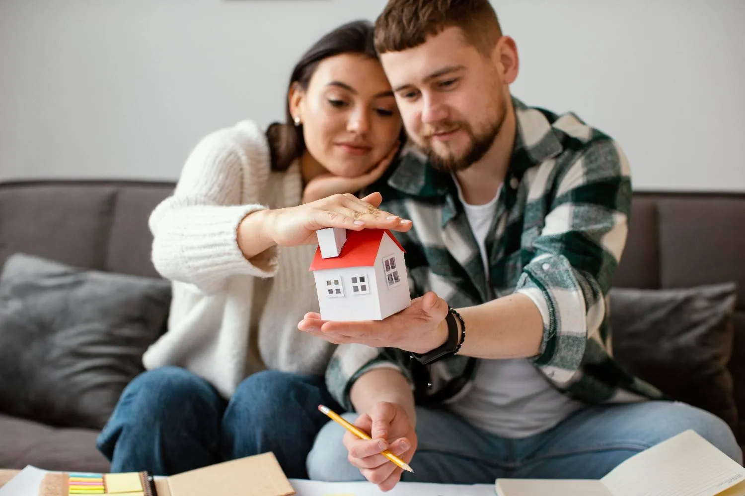 Couple holding a model house while going through their home cover